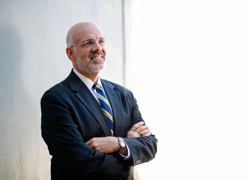 Joe DiPietro dressed in a suit standing against a wall with his arms folded
