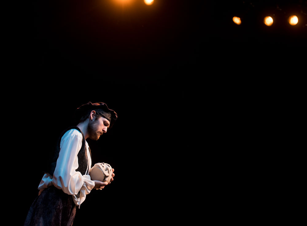 A young man in costume cradling a skull on a darkened stage